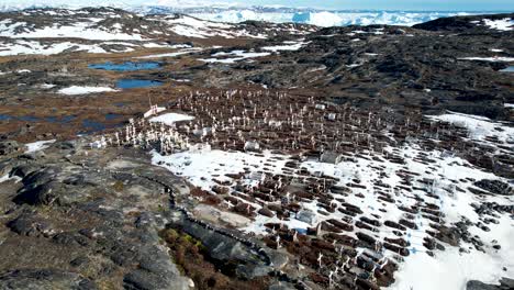 Dramatic-aerial-view-over-white-crosses,-grave-stones-in-small-cemetery-to-bay-of-melting-icebergs