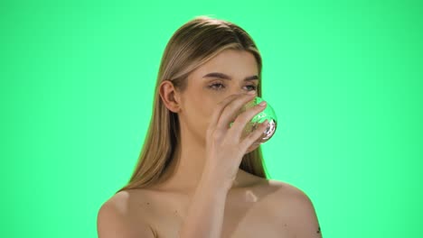Medium-slow-motion-shot-of-a-young-woman-with-full-beautiful-lips-drinking-a-glass-of-water-to-quench-her-thirst-against-green-background
