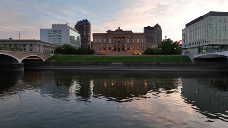 Aerial-glide-over-Des-Moines-River-looking-towards-World-Food-Prize-Hall-of-Laureates-and-skyline-during-beautiful-summer-sunset