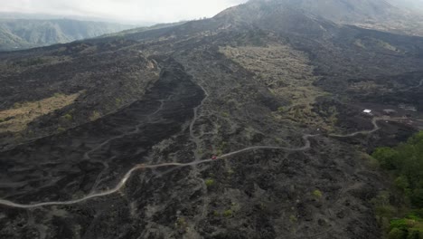 Aerial-tracks-truck-driving-on-road-across-Mount-Batur-lava-field