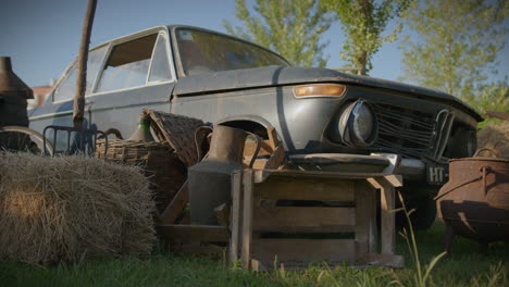 Old-And-Rusty-Car-Wide-Low-Angle-Shot-Surrounded-By-Rustic-Farm-Tools