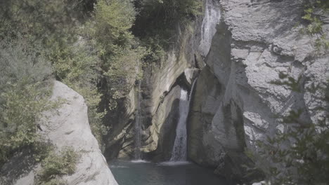 Aufnahme-Des-Wasserfalls-In-Der-Nähe-Von-Bogova,-Albanien,-An-Einem-Sonnigen-Tag-Ohne-Menschen-Und-Klarem-Wasser-Mit-Felsen-Und-Pflanzen-Rund-Um-Den-Baumstamm