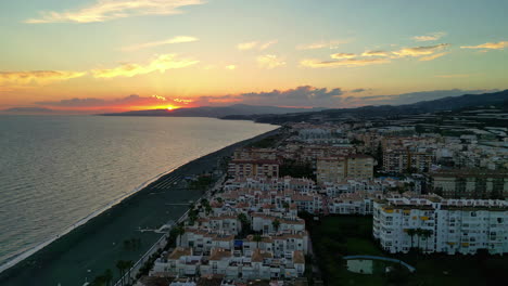 Golden-sun-setting-down-over-exotic-coast-township-in-Spain,-aerial-view