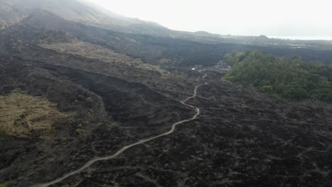 Lone-vehicle-drives-on-dirt-road-across-volcanic-lava-field-in-Bali