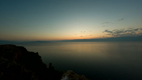 Zeitraffer-Eines-Sonnenaufgangs-In-Albanien-Am-Morgen,-Der-An-Einem-Klaren-Tag-Mit-Orangefarbenem-Himmel-über-Das-Wasser-Wacht,-Mit-Den-Bergen-Mazedoniens-Im-Hintergrund