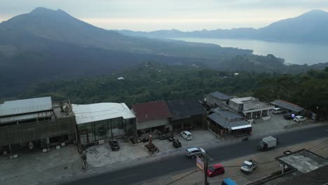 Hazy-aerial-overlooks-clifftop-buildings-to-distant-Mount-Batur,-Bali