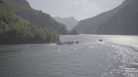 Eine-Fährfahrt-In-Albanien-Von-Fierze-Nach-Koman-über-Den-See-Mit-Einer-Majestätischen-Natur-Rundherum-An-Einem-Sonnigen-Tag-Mit-Wolken,-Die-über-Den-Fluss-Blicken,-Während-Zwei-Boote-Mit-Hoher-Geschwindigkeit-Vorbeifahren-Und-Vorwärts-Fahren