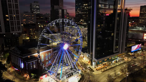 Hyperlapse-drone-shot-of-rotating-Skyview-Atlanta-Ferris-Wheel-and-traffic-on-downtown-road-in-town-during-golden-hour--rising-time-lapse