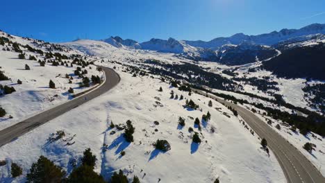 Aerial-drone-view-of-a-scenic-road-running-through-a-snow-covered-mountain-landscape