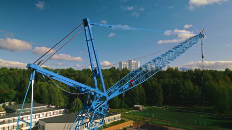 Rear-strut,-front-strut,-jib-and-pendant-of-a-blue-luffing-construction-crane-against-a-blue-sky-and-clouds-with-forest-in-background