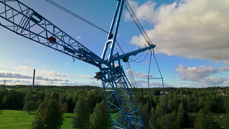 Rear-strut-and-front-strut-of-a-blue-luffing-construction-crane-against-a-blue-sky-and-clouds-with-forest-in-background