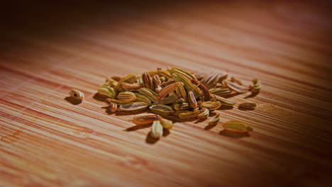 Fennel-seeds-on-a-wooden-surface-with-dramatic-lighting,-camera-orbiting