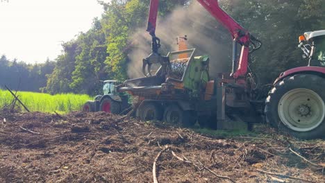 Farmer-using-grabber-on-end-of-hydraulic-arm-to-feed-wood-and-vegetation-into-a-shredder