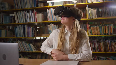 Una-Adolescente-Usando-Una-Computadora-Portátil-Y-Gafas-De-Realidad-Virtual-En-La-Biblioteca,-De-Mano