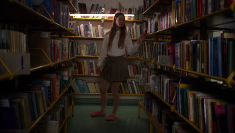 Schoolgirl-enjoying-the-school-library,-walking-among-bookshelves,-handheld-shot
