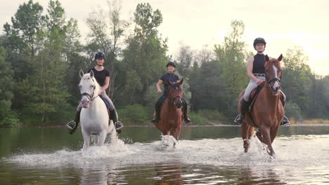 Three-rider-girls-crossing-the-river-riding-their-horses,-handheld-shot