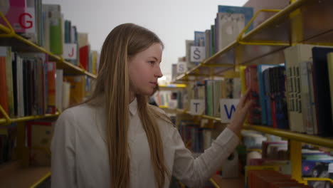 Teenage-girl-searching-for-a-book-in-library-bookcases,-handheld-close-up-shot