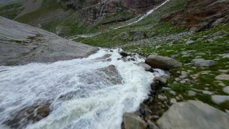 Racing-drone-flying-over-water-stream-flowing-at-Fellaria-glacier-in-Valmalenco-of-Valtellina,-Italy