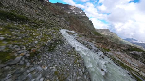 Fpv-racing-drone-flying-over-water-stream-flowing-at-Fellaria-mountain-glacier-in-Valmalenco-of-Valtellina,-Italy