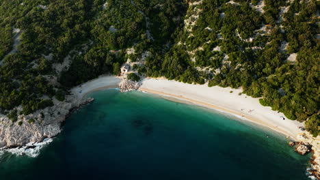 Drone-descends-tilting-up-as-waves-crash-on-white-sand-of-Lubenice-beach-Croatia,-gorgeous-lagoon