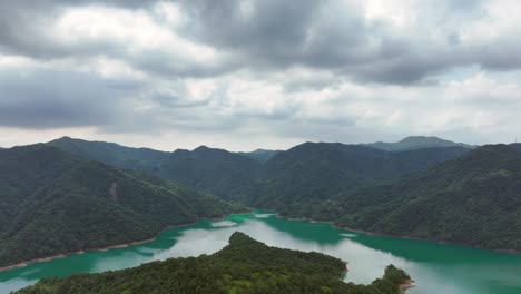 Drone-flight-over-Feitsui-Reservoir-with-mountain-range-and-green-colored-water-at-cloudy-day---Green-overgrown-hills-in-wilderness-of-Taiwan