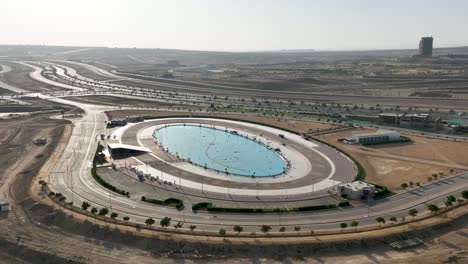 Aerial-drone-panoramic-shot-of-an-oval-water-fountain-beside-a-highway-in-the-town-of-Bahria-in-Karachi,-Pakistan