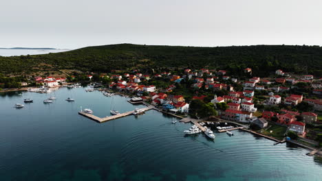Drone-rises-above-port-harbor-of-Ilovik-island-Croatia-establishing-stunning-summer-waters-and-village