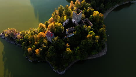 Aerial-overview-of-incredible-Ottenstein-castle-in-middle-of-reservoir,-golden-glow-illuminates-autumn-yellow-trees