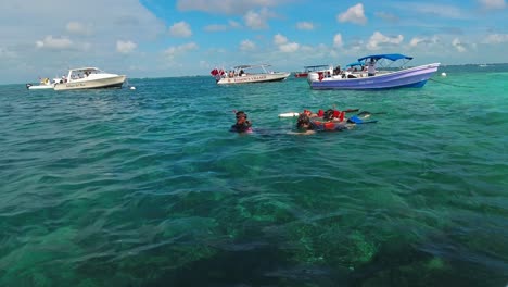 Tourist-boats-float-off-the-tropical-waters-off-Hol-Chan-Marine-Reserve,-San-Pedro,-Belize,-while-snorkellers-swim-nearby