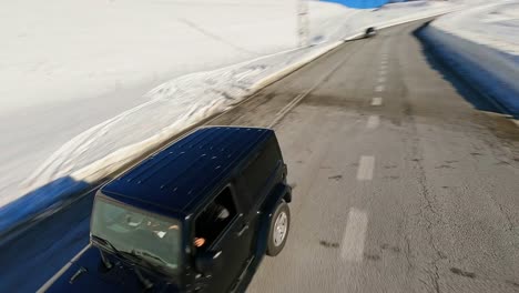 FPV-aerial-drone-tracking-a-Jeep-driving-along-a-picturesque-highway-in-the-winter-landscape-of-the-Pyrenees-Mountains