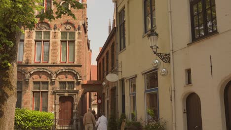 Old-Couple-Walking-Through-Brick-Architectures-In-Historic-Village-In-Bruges,-Belgium