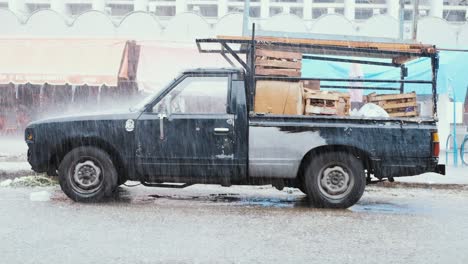 Side-shot-of-a-vintage-truck-in-slow-motion,-getting-hit-by-fierce-rain,-illustrating-the-synergy-of-transportation-and-nature’s-elements