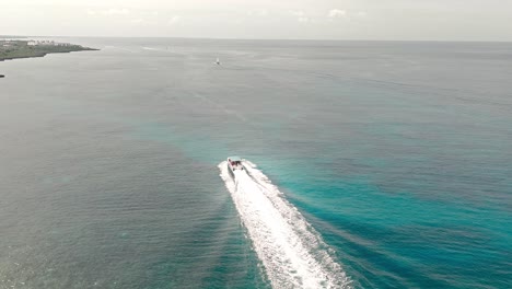 Long-white-wake-trail-of-speedboat-cruising-over-calm-sea-water-along-Bayahibe-coast,-La-Romana-in-Dominican-Republic