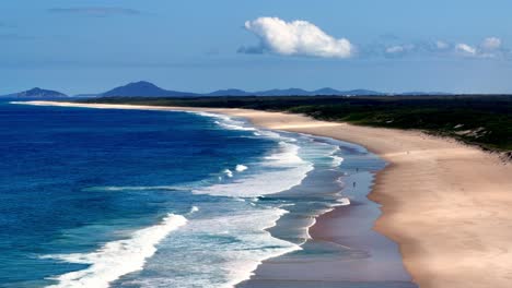 Ein-Strand-Mit-Einem-Sandstrand-Und-Einem-Sandstrand-Daneben-Und-Einem-Blauen-Ozean-Mit-Weißen-Wellen-Aus-Der-Vogelperspektive
