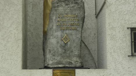 A-stone-monument-with-the-masonic-symbols-of-the-square,-the-compass-and-the-letter-G-and-above-a-phrase-in-Spanish-translated-to-"Man,-architect-of-his-own-destiny"