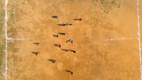 4K-Cinematic-sport-aerial-drone-footage-of-children-playing-on-a-footbal-field-in-the-mountain-village-of-Doi-Pui-next-to-Chiang-Mai,-Thailand-on-a-sunny-day