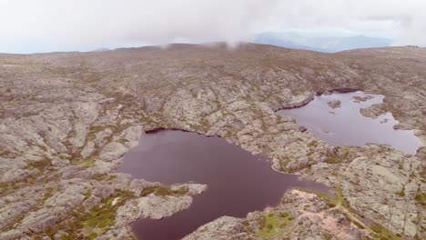 Aerially-capturing-the-panoramic-view-of-the-highest-point-in-Serra-de-Estrella,-including-the-lake-formation-and-surrounding-landscape