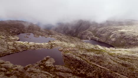Using-a-drone,-slow-motion-footage-captures-the-lake-perched-atop-the-highest-point-of-Serra-de-Estrella,-as-clouds-gently-obscure-the-mountain