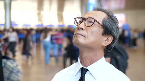 A-Japanese-businessman-stands-at-Ben-Gurion-Airport-in-Israellooking-at-the-arrivals-and-departures-board-He-is-photographed-from-the-front-with-reflecting-in-his-glasses