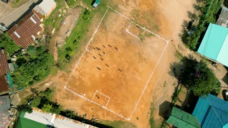 4K-Filmaufnahmen-Von-Sportdrohnen-Aus-Der-Luft-Von-Kindern,-Die-An-Einem-Sonnigen-Tag-Auf-Einem-Fußballplatz-Im-Bergdorf-Doi-Pui-Neben-Chiang-Mai,-Thailand,-Spielen