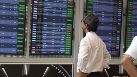 A-Japanese-businessman-stands-at-Ben-Gurion-Airport-in-Israel,-gazing-at-the-arrivals-and-departures-board