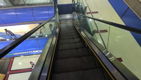 POV-Aufnahme-Eines-Automatischen-Stufenaufzugs,-Kamera-Fährt-Die-Automatische-Treppe-Hinunter,-Wo-Menschen-Im-Einkaufszentrum-Einkaufen