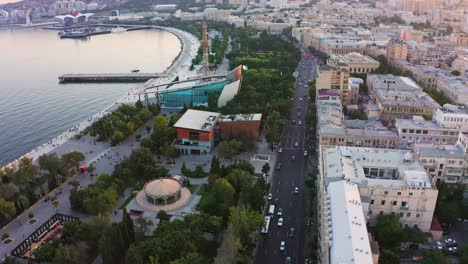 Aerial-–-Natural-parkland-along-the-coastline-and-streets-of-Baku-old-town-after-sunset,-Azerbaijan