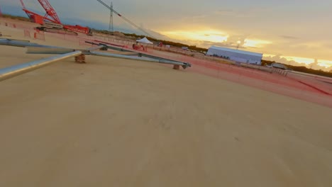 FPV-Drone-shot-flying-through-steel-structures-at-a-construction-area,-during-sunset