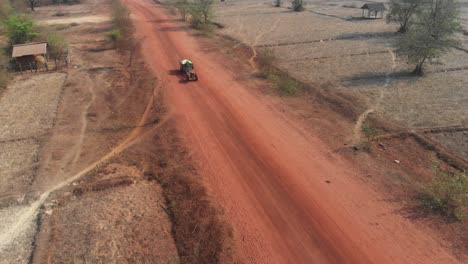 Tractor-with-trailer-driving-on-dirt-road-at-Loas,-aerial