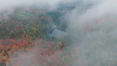 Drone-Flies-Through-Misty-Clouds-to-Reveal-Autumn-Forest-and-Pond-in-the-Center