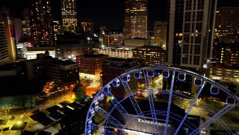 Ascending-drone-shot-showing-blue-colored-Skyview-Atlanta-and-beautiful-skyline-with-skyscraper-buildings-in-background-during-dark-night,America