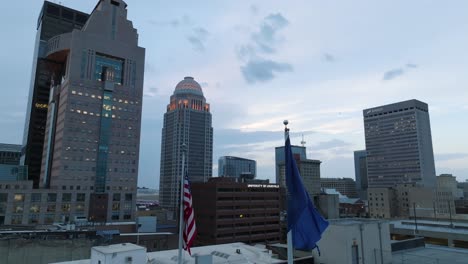American-and-Kentucky-flags-waving-in-front-of-downtown-Louisville,-KY-skyline-at-dawn