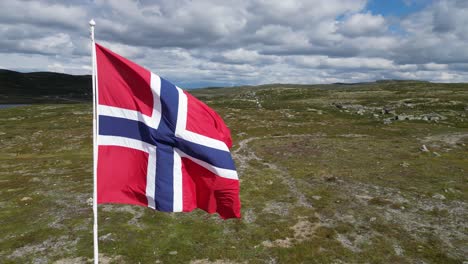 Norwegian-flag-waving-in-the-wind-in-Hardangervidda-National-Park,-Norway---Aerial-Circling