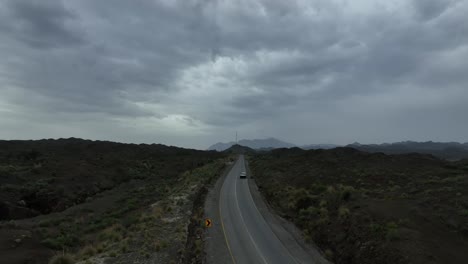 Aerial-drone-shot-of-a-highway-with-a-vehicle-moving-on-the-road-and-wast-landscape-and-dark-clouds-on-the-sky